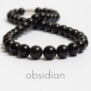 Puede incluir: Un collar de cuentas de obsidiana negra. Las cuentas son redondas y lisas, y el collar está encordado en un cordón plateado.