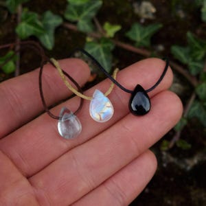 Puede incluir: Tres colgantes de cristal en forma de lágrima en cordones marrones y negros. Los colgantes están hechos de piedras transparentes, blancas y negras.