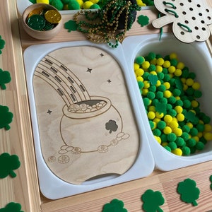 Peut inclure: Un ensemble de jeu en bois avec un pot d'or au bout d'un arc-en-ciel, un bol de pièces d'or et un récipient rempli de pompons verts et jaunes.