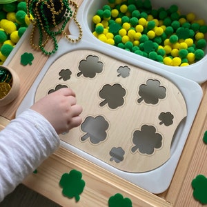 Peut inclure: Un plateau en bois avec des formes de trèfles découpées. La main d'un enfant atteint le plateau. Il y a des trèfles verts éparpillés sur une surface en bois.