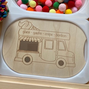 May include: A wooden play food truck with a white background. The truck has a window, a door, and wheels. The text "glace - gaufre - crepe - bonbon" is written on the truck.