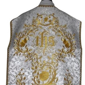 May include: White liturgical vestment with gold embroidery featuring a floral design and the letters "IHS".