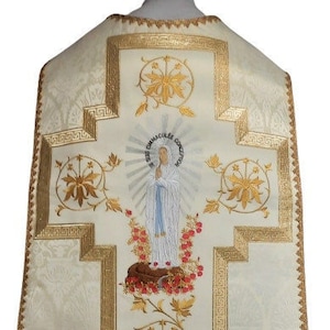 May include: White liturgical vestment with gold embroidery featuring a cross and a depiction of the Virgin Mary. The embroidery includes floral motifs and a Greek key border.