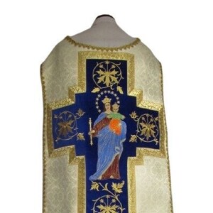 May include: A white and gold embroidered chasuble with a blue velvet cross featuring a depiction of the Virgin Mary and baby Jesus. The cross is surrounded by gold floral designs.