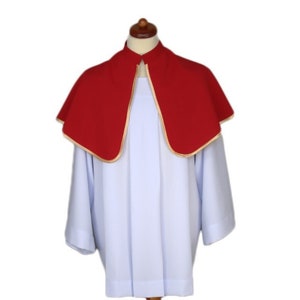 May include: A white liturgical robe with a red cape featuring a gold trim. The robe is displayed on a wooden stand.