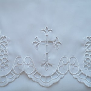 Peut inclure: Tissu blanc brodé avec des motifs de croix et de vignes. Le tissu a un bord festonné.