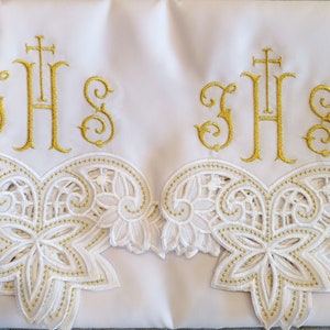 Puede incluir: Dos paneles de tela blanca con ribete de encaje bordado en oro y las letras "IHS" en bordado dorado.