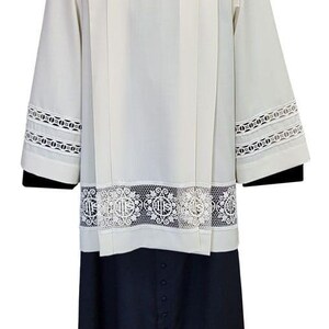May include: A white cassock with a black collar and lace trim. The cassock has a pleated front and a black cassock underneath.