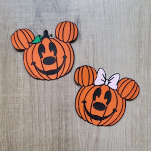 Pode incluir: Duas decorações em forma de abóbora laranja com rostos de Mickey Mouse e Minnie Mouse. A abóbora do Mickey Mouse tem um caule verde e a abóbora da Minnie Mouse tem um laço rosa.