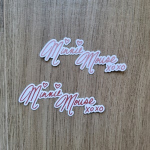 May include: Two white stickers with pink glitter lettering that reads "Minnie Mouse xoxo".