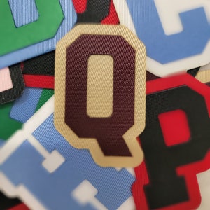 Peut inclure: Gros plan sur un tas de lettres en feutre de différentes couleurs, notamment vert, rouge, bleu, noir et blanc. Les lettres sont disposées dans un ordre aléatoire, avec la lettre "Q" au centre.