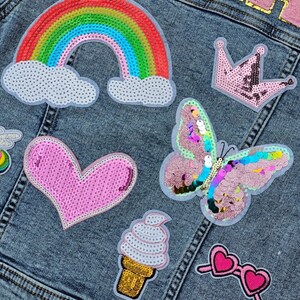 May include: A denim jacket with colourful sequined patches, including a rainbow, a heart, a butterfly, a crown, an ice cream cone, and sunglasses.