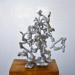 May include: A silver aluminum sculpture resembling a tree with intricate branches, displayed on a wooden base.