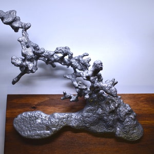 May include: A silver aluminum ant farm sculpture mounted on a dark brown wooden base. The sculpture is shaped like a tree with branches and leaves.