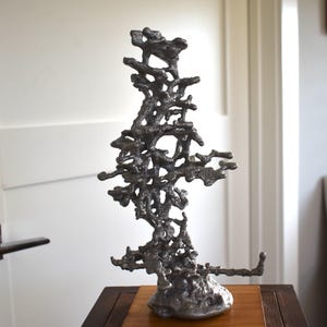 May include: A silver metal sculpture of a tree with a unique, organic, and intricate design. The sculpture is made of aluminum and has a smooth, polished finish.
