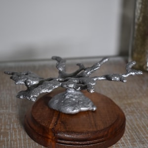 May include: A silver metal sculpture of a tree branch, with a textured surface, on a wooden base.