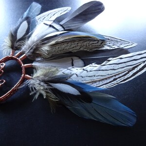 May include: A copper wire ear cuff with a cluster of blue, white, and black feathers attached. The feathers have a striped pattern.