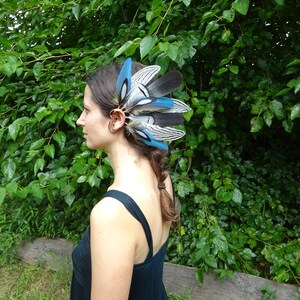 May include: A woman wearing a black dress with a blue and white feather ear cuff. The ear cuff is made of feathers and has a blue and white color scheme.