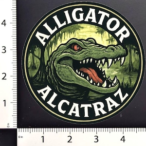 May include: A set of round stickers featuring a detailed illustration of an alligator with red eyes and an open mouth, set against a swamp scene. The text "ALLIGATOR ALCATRAZ" is in a circular design.