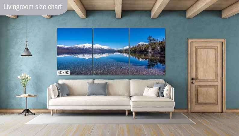 May include: A three-panel canvas print of a mountain lake with snow-capped mountains reflected in the water. The print is 40 inches by 90 inches and is hanging on a wall in a living room.