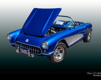 May include: A classic blue 1957 Chevrolet Corvette convertible with the hood open, revealing the engine. The car has a white license plate that reads "57 CRUISR".
