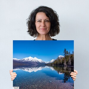 May include: A photograph of a mountain range reflected in a still lake. The mountains are snow-capped and the sky is a bright blue. The lake is a clear blue and the water is calm. The photo is printed on a 16x20 inch canvas.
