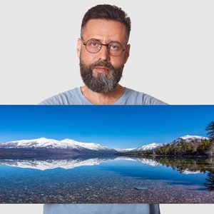 May include: A panoramic photo of a snow-capped mountain range reflected in a still lake. The sky is a bright blue, and the water is clear and calm. The photo is labeled "1x3" in the bottom left corner.