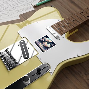 May include: A yellow electric guitar with a white pickguard and a sticker of a cloudy sky on the pickguard. The guitar has a black pickup and a black knob.