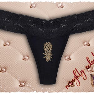 Puede incluir: Braga tanga negra con un diseño de piña dorada con purpurina. El borde superior presenta un ribete de encaje negro. Las palabras "naughty eclectics" están escritas en rojo en el fondo.