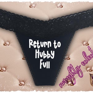 Op de afbeelding: Zwarte string met een kanten rand aan de bovenkant. De tekst "Return to Hubby Full" is wit op de voorkant gedrukt. De afbeelding heeft een roze achtergrond met een decoratieve rand.