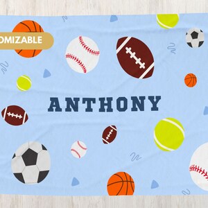 May include: A blue personalized sports themed blanket with the name Anthony printed in navy blue. The blanket features a variety of sports balls including baseballs, basketballs, footballs, soccer balls, and tennis balls.