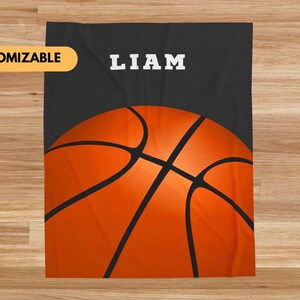 Può includere: Una coperta da basket nera e arancione con il nome "LIAM" in testo bianco.