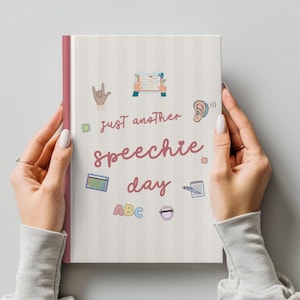 以下が含まれることがあります： ライトグレーのストライプ柄の表紙に、ピンクの筆記体で「just another speechie day」と書かれたノート。表紙には、ハンドサイン、開いた本、耳、グリッド、メモ帳、ABCの文字、口などのカラフルなイラストが描かれています。