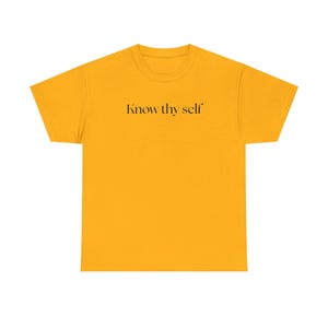 Può includere: T-shirt giallo senape con la scritta "Know thy self" stampata in nero. La maglietta ha un girocollo e maniche corte. Il tessuto sembra essere un morbido misto cotone.