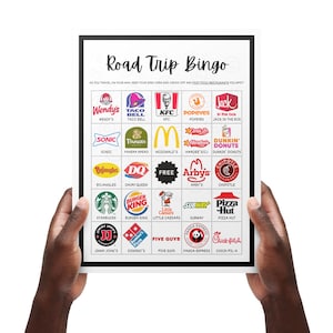 May include: A white framed "Road Trip Bingo" game board featuring fast food restaurant logos. Includes Wendy's, Taco Bell, KFC, Popeyes, Sonic, Panera Bread, McDonald's, Hardee's, Dunkin' Donuts, and more. Held by two hands.