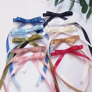 May include: A selection of satin ribbon bows in a range of colours, such as blue, pink, green, gold, and red. Each bow is crafted with matching ribbon tails, producing a delicate and decorative appearance. Ideal for crafts, gift wrapping, or embellishments.