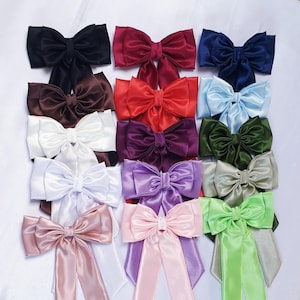 May include: An assortment of satin bows in a range of colours, such as black, burgundy, navy, brown, red, light blue, purple, olive green, lavender, pink, and light green. Some bows have long tails. The bows are displayed on a white background.