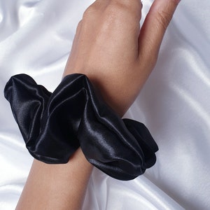 A close up photo of the medium black satin scrunchie worn on the wrist as an accessory