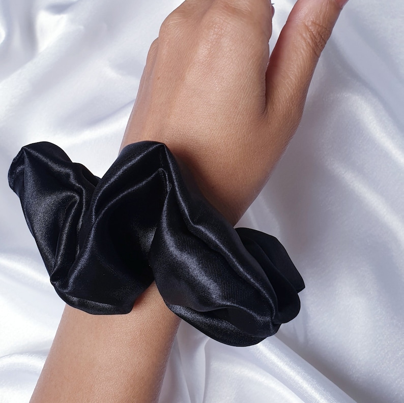 A close up photo of the medium black satin scrunchie worn on the wrist as an accessory