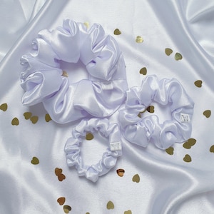 May include: Three white satin scrunchies of different sizes. The scrunchies are on a white satin background with gold glitter hearts.