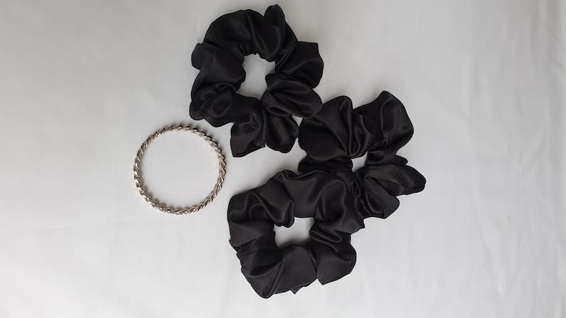 Photo of 3 medium black satin scrunchies placed together next to a bangle for size reference