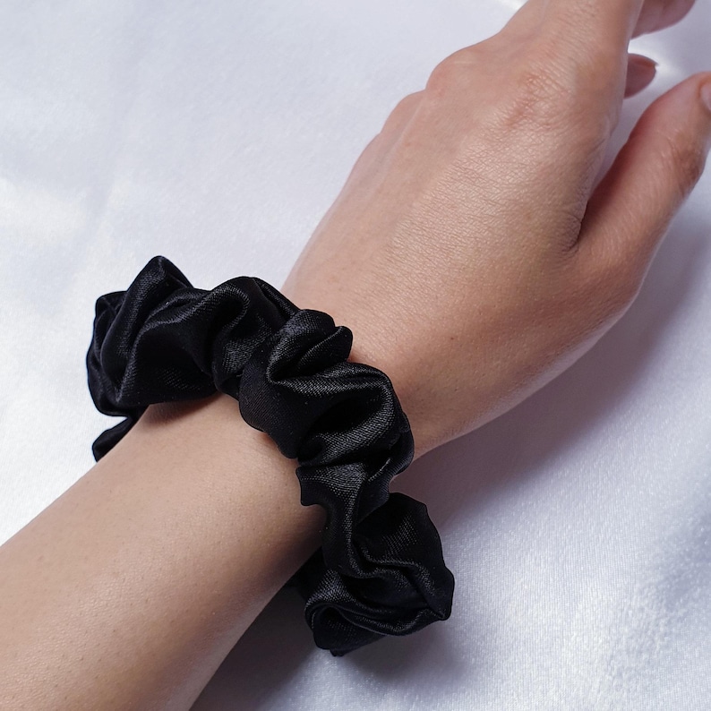 A photo of the mini black satin scrunchie worn on the wrist as a fashion accessory