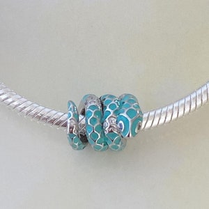 May include: A silver charm bracelet with a blue and silver charm and a turquoise and silver charm. The bracelet is on a white background.
