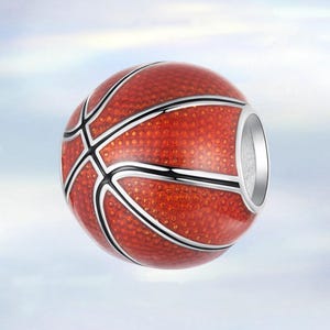 Può includere: Un charm a forma di pallone da basket con un accento in metallo color argento. Il charm è principalmente arancione con linee nere e bianche, che imitano il design di un pallone da basket. Il charm è progettato per essere un ciondolo o una perlina.