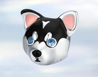 Könnte beinhalten: Ein silberner Charm in Form eines Hundekopfes. Der Hund hat schwarzes Fell oben, rosa Ohren und blaue Augen. Der Charm hat eine kleine schwarze Nase und ein kleines weißes Dreieck auf der Stirn.