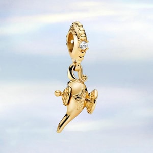 Op de afbeelding: Een goudkleurige bedel in de vorm van een toverlamp, met ingewikkelde details en een kleine, heldere edelsteen. De bedel hangt aan een decoratieve ring, waardoor een hanger ontstaat. De algehele esthetiek is elegant en gedetailleerd.