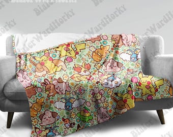 May include: A soft, light green blanket featuring a repeating pattern of cartoon characters, flowers, and clouds. The blanket is draped over a gray sofa. The characters are in shades of yellow, pink, orange, and blue.