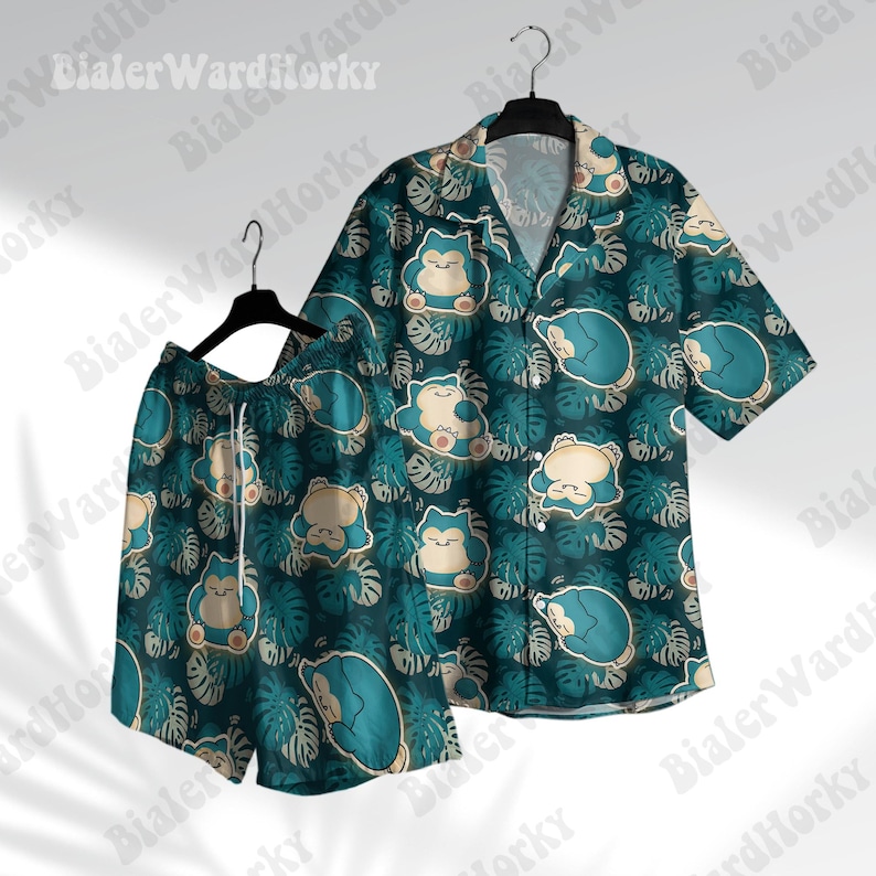 May include: A teal and beige matching shirt and shorts set. The set features a pattern of a cartoon character and tropical leaves. The shirt has short sleeves and a button-down design. The shorts have a drawstring waist. The set is hanging on a black hanger.