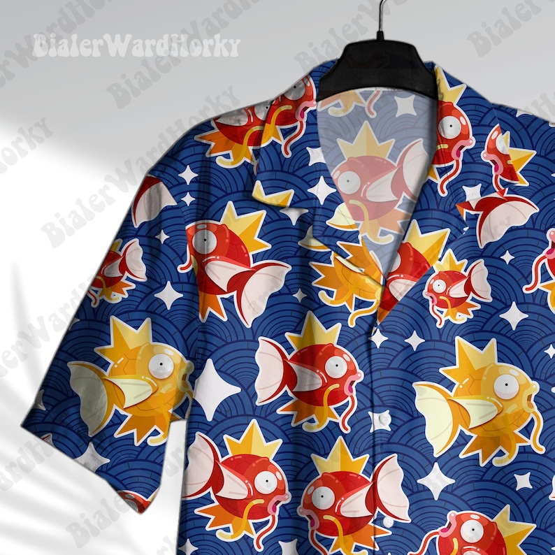 May include: A blue short-sleeved button-up shirt with a repeating pattern of orange and red fish with yellow crowns on a blue background. The shirt has a white collar and white buttons.