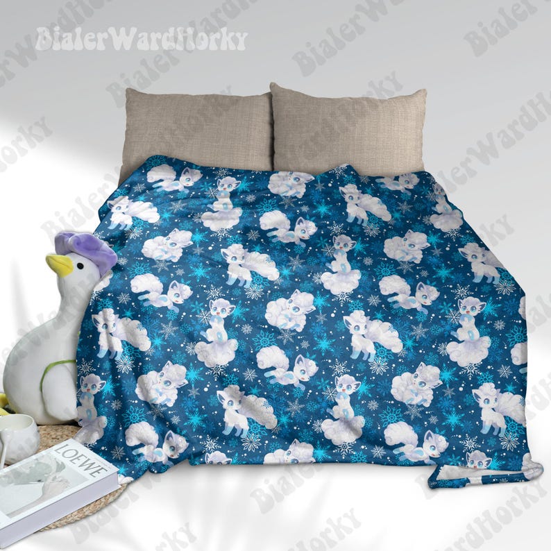 May include: A blue blanket featuring a pattern of white cartoon foxes, clouds, and snowflakes. The blanket is draped over a bed with two beige pillows. The blanket is made of a soft material.